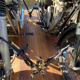 Two motorcycles secured with black and blue straps on a wooden deck floor outdoors.