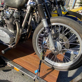 Close-up of a Yamaha motorcycle on a wooden flatbed trailer, showing the front wheel, fork, engine, and trailer deck in outdoor daylight.